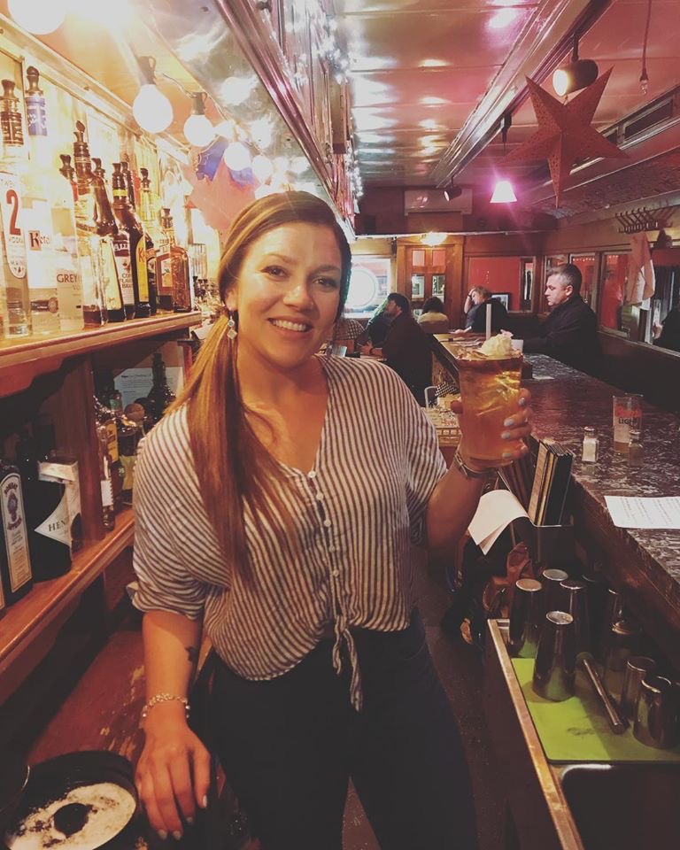 A smiling bartender holding up a drink behind the bar