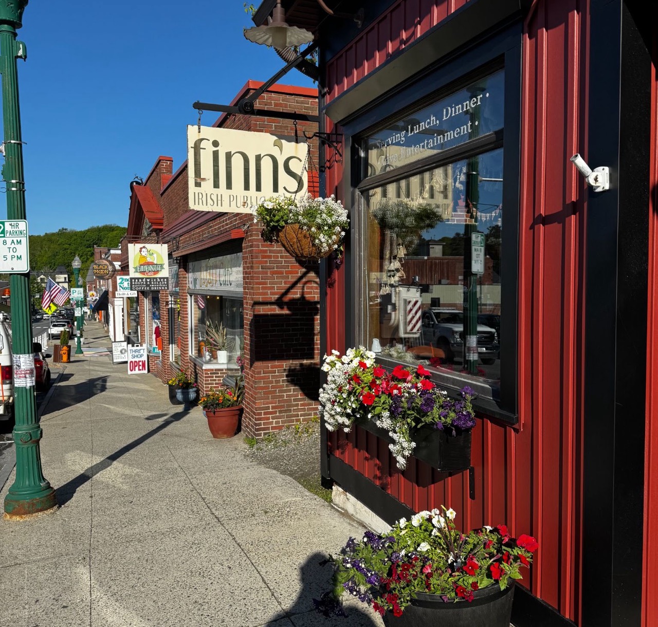 The Main Street sidewalk along the red storefront, with the hanging sign and flower planters