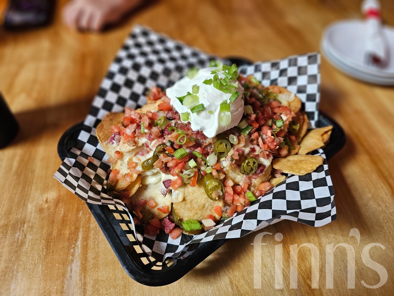 A checkered basket of loaded chips topped with salsa, jalapeños, green onion and sour cream